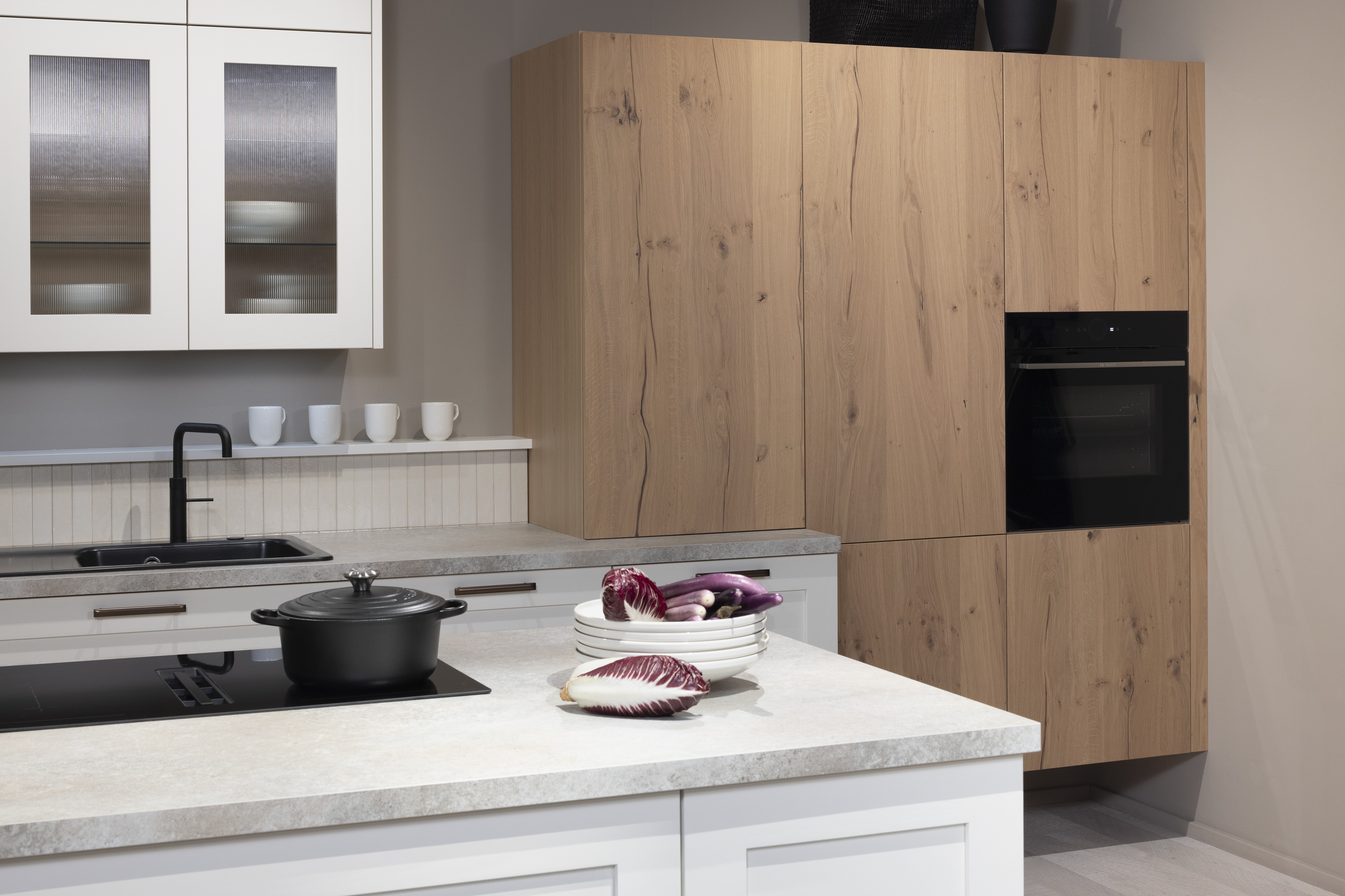 APL: 15 Kalkstein Repro 25 mm Front: AV 6055 Weiß Echtholz lackiert,  Front 2: AV 6082 Wildeiche-natur Korpus: 2085 Designkorpus Feineiche-natur Griff: 515 Metall Bronze-dunkel Geräte: Bosch  Armatur: Quooker Spüle: Systemceram   Features: Landhausküche modern, Echtholz RAL und NCS lackierbar, Riffelglasvitrine, Beleuchtung, schwebender Block, Echtholzfurnier lackiert kombiniert mit Echtholzfurnier, Fliesen, Korpus Echtholz Feineiche Natur, Griffe in Bronze. 