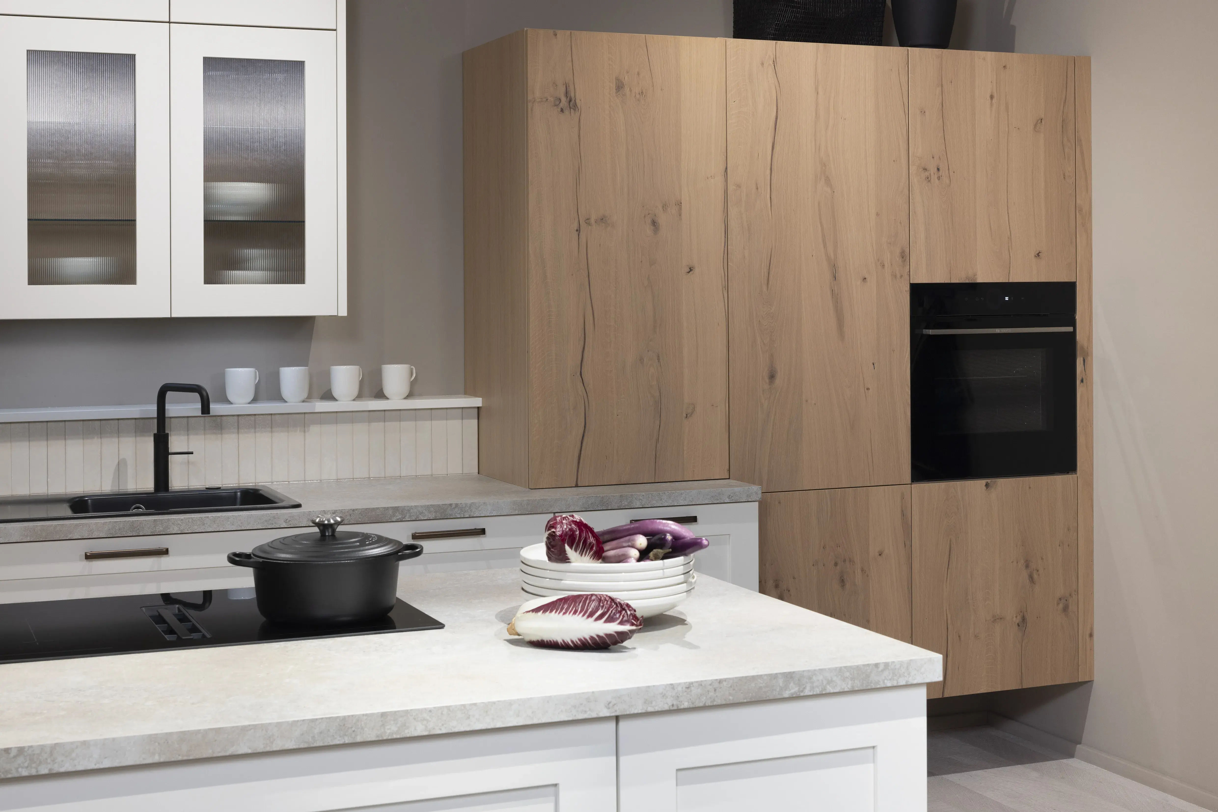 APL: 15 Kalkstein Repro 25 mm Front: AV 6055 Weiß Echtholz lackiert,  Front 2: AV 6082 Wildeiche-natur Korpus: 2085 Designkorpus Feineiche-natur Griff: 515 Metall Bronze-dunkel Geräte: Bosch  Armatur: Quooker Spüle: Systemceram   Features: Landhausküche modern, Echtholz RAL und NCS lackierbar, Riffelglasvitrine, Beleuchtung, schwebender Block, Echtholzfurnier lackiert kombiniert mit Echtholzfurnier, Fliesen, Korpus Echtholz Feineiche Natur, Griffe in Bronze. 